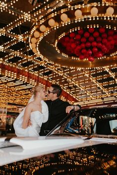 a bride and groom standing in front of a car with lights on the ceiling behind them