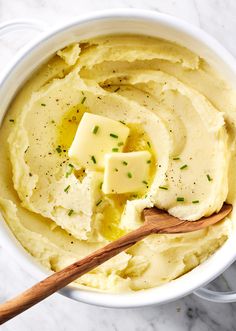 mashed potatoes with butter and parsley in a white bowl on a marble surface