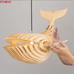 a woman holding a wooden light fixture with a whale tail design on it's side