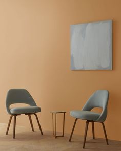 two chairs and a table in front of an orange wall with a painting on it