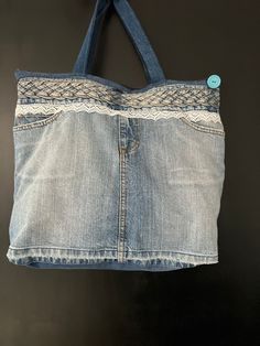 an old jean purse hanging from a hook on a black wall with a blue button