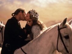 a man and woman kissing on the back of a white horse in front of an orange sky