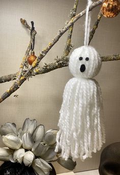 a white stuffed animal hanging from a tree branch next to a potted plant with flowers