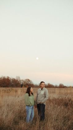 a man and woman standing in the middle of a field with a kite flying overhead