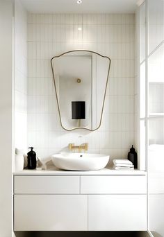 a bathroom with a sink, mirror and black vases on the counter top in front of it