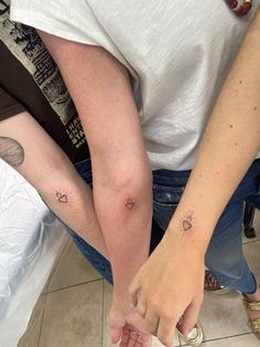 two people with tattoos on their arm and one holding the other's hand while sitting down