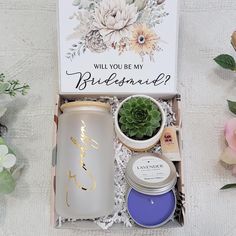 an open box containing candles and flowers on a white tablecloth with the words will you be my bridesmaid?