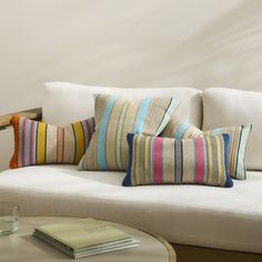 a white couch with colorful striped pillows and a book on the table next to it