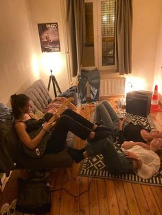 two women are sitting on the floor playing guitars and singing to another woman who is laying down