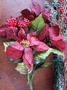 the poinsettis and greenery are arranged on the wooden table with red berries