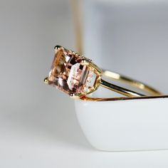 Beautiful emerald cut peachy pink color morganite ring, diamond hidden halo ring. DETAILS ABOUT THE RING!* 9x7mm emerald cut morganite is peach pink color.* Ring band is 1.3mm 14k solid yellow gold* Emerald cut 4 prong setting is 14k solid yellow gold* Set 20 white diamonds in the hidden halo, total 0.05 ct. weight. *** All our raw materials are sourced from US-based companies for the quality and safety of our handmade products.*** this ring is handcrafted for you in our local studio in Redlands Peach Pink Color, Hidden Halo Ring, Topaz Jewelry, Tourmaline Jewelry, Aquamarine Jewelry, Garnet Jewelry, Aesthetic Pastel, Yellow Gold Setting, Morganite Ring