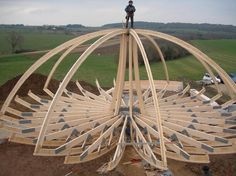 a man standing on top of a large wooden structure in the middle of a field