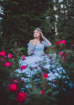 a woman in a blue dress is standing among pink flowers and trees with her hand on her head