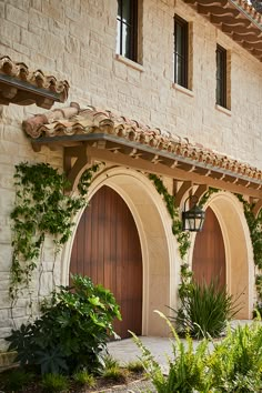 a building with two brown doors and green plants in the front yard on either side