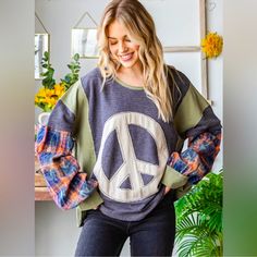 a woman standing in front of a window wearing a peace sign sweater with plaid sleeves