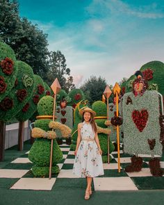 a woman wearing a hat standing in front of topiary plants at the epcoti garden