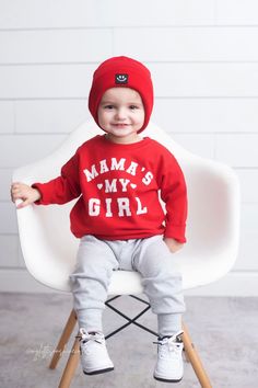 a little boy sitting on top of a white chair wearing a red sweater and hat