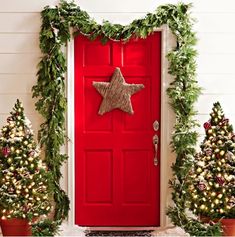 a red door decorated with christmas trees and greenery next to it is a star