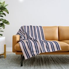 a tan leather couch with a blue and white striped blanket on it next to a potted plant