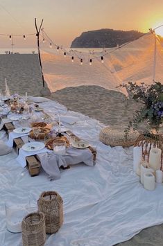 a table set up on the beach with food and candles for an outdoor dinner party