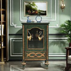 a green cabinet with two swans on it in front of a painting and bookshelves