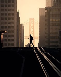 a man walking across a bridge in front of tall buildings with the golden gate bridge in the background