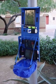 a blue toilet sitting on top of a metal pole next to a tree and bushes