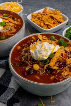 three bowls of chili and cheese soup with tortilla chips on the side next to it