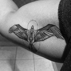 a black and white photo of a bird tattoo on the right arm, with wings spread out