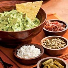 bowls filled with guacamole, beans and tortilla chips on a table