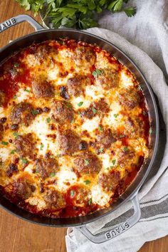 a pizza with meatballs and cheese in a pan on a wooden table next to some parsley