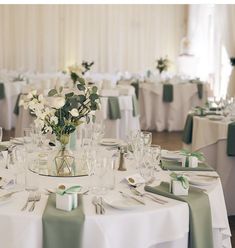 the table is set with white and green flowers in vases, napkins, and silverware