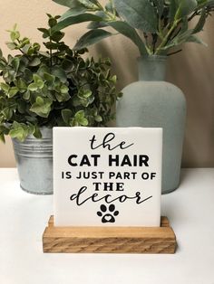 a sign that says the cat hair is just part of the decor next to some potted plants