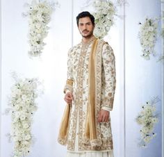 a man standing in front of a white and gold wedding arch with flowers on it