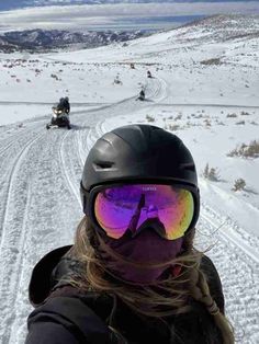 a woman wearing ski goggles while standing in the snow with two atvs behind her