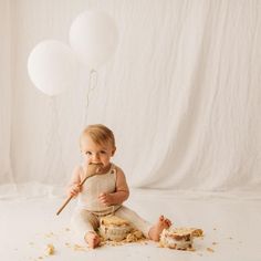 a baby is sitting on the floor eating cake and holding a wooden spoon in his mouth