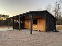 a horse barn with the doors open in an empty lot