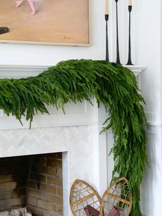 a mantel decorated with greenery and wicker chairs in front of a fireplace