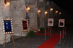 some lights that are on the side of a building near a red carpet and fence