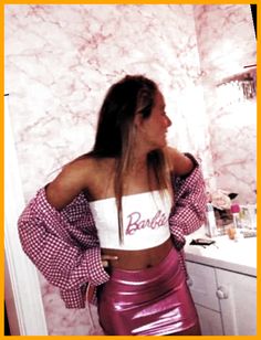 a woman standing in front of a mirror wearing a pink and white crop top with the word barbie written on it