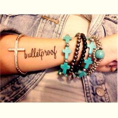 a woman wearing bracelets with crosses on her arm and the word bulletproof written on it