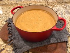 a red pot filled with soup on top of a wooden cutting board