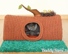 a cat is sitting in a crocheted bed with a plant on top of it