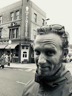 a man standing in front of a tall building on a street with people walking by