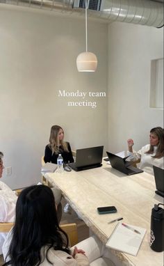 three women sitting at a table with laptops in front of them and the words monday team meeting written on the wall