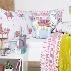 a bed with colorful pillows and blankets on top of it next to a white table