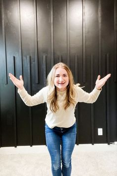 a woman standing in front of a black wall with her hands out to the side