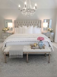 a white bed sitting in a bedroom next to a chandelier and two tables