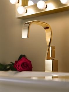 a gold faucet with a red rose in the corner and a white wall behind it