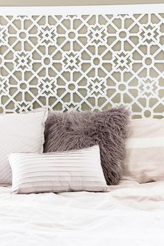 a bed with white sheets and pillows in front of a decorative headboard on the wall